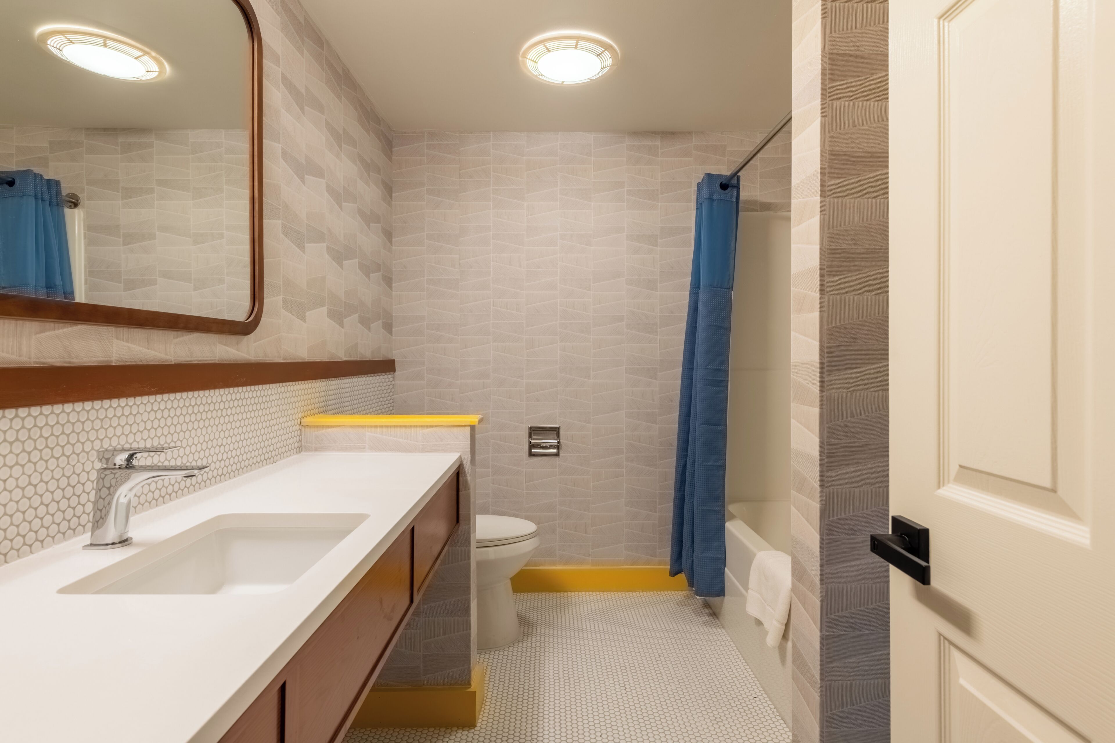 Une salle de bain avec un lavabo blanc, un miroir et des toilettes, des carreaux à motifs et un rideau de douche bleu.