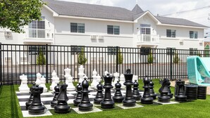 A large outdoor chess set on a grassy lawn with a white house in the background. - Driftaway Hotel and Pool (Ogunquit)