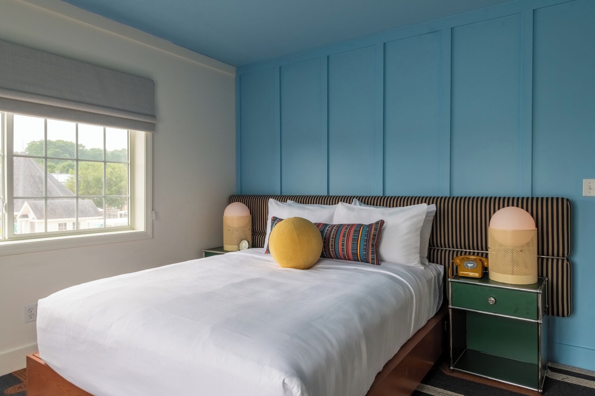 A bedroom with a large bed, a window, a green nightstand, and a blue wall.