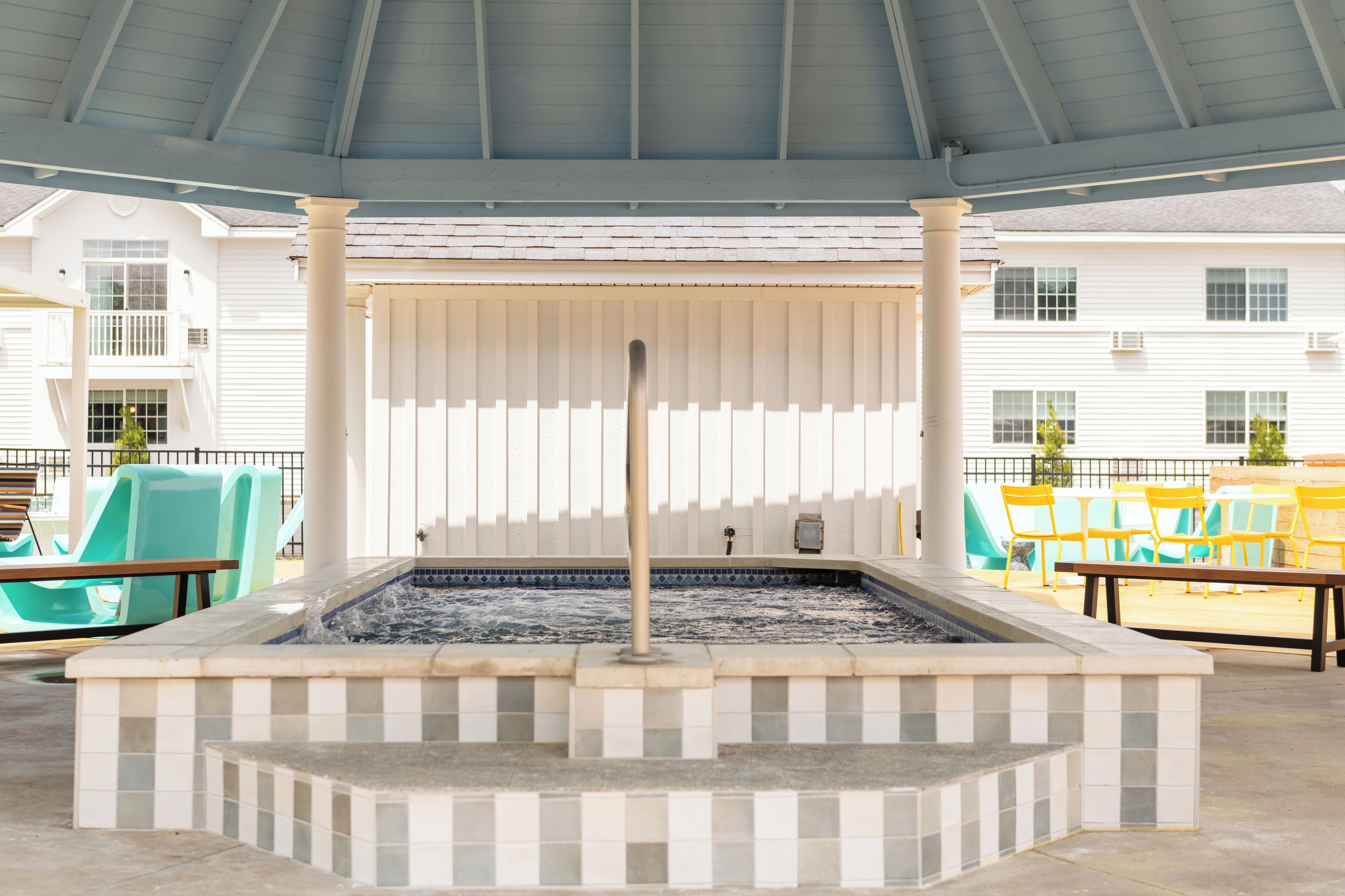 An outdoor hot tub area with tiled flooring, a metal pole, and yellow chairs.