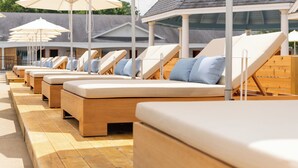 A row of sun loungers with cushions, wooden flooring, and white umbrellas. - Driftaway Hotel and Pool (Ogunquit)