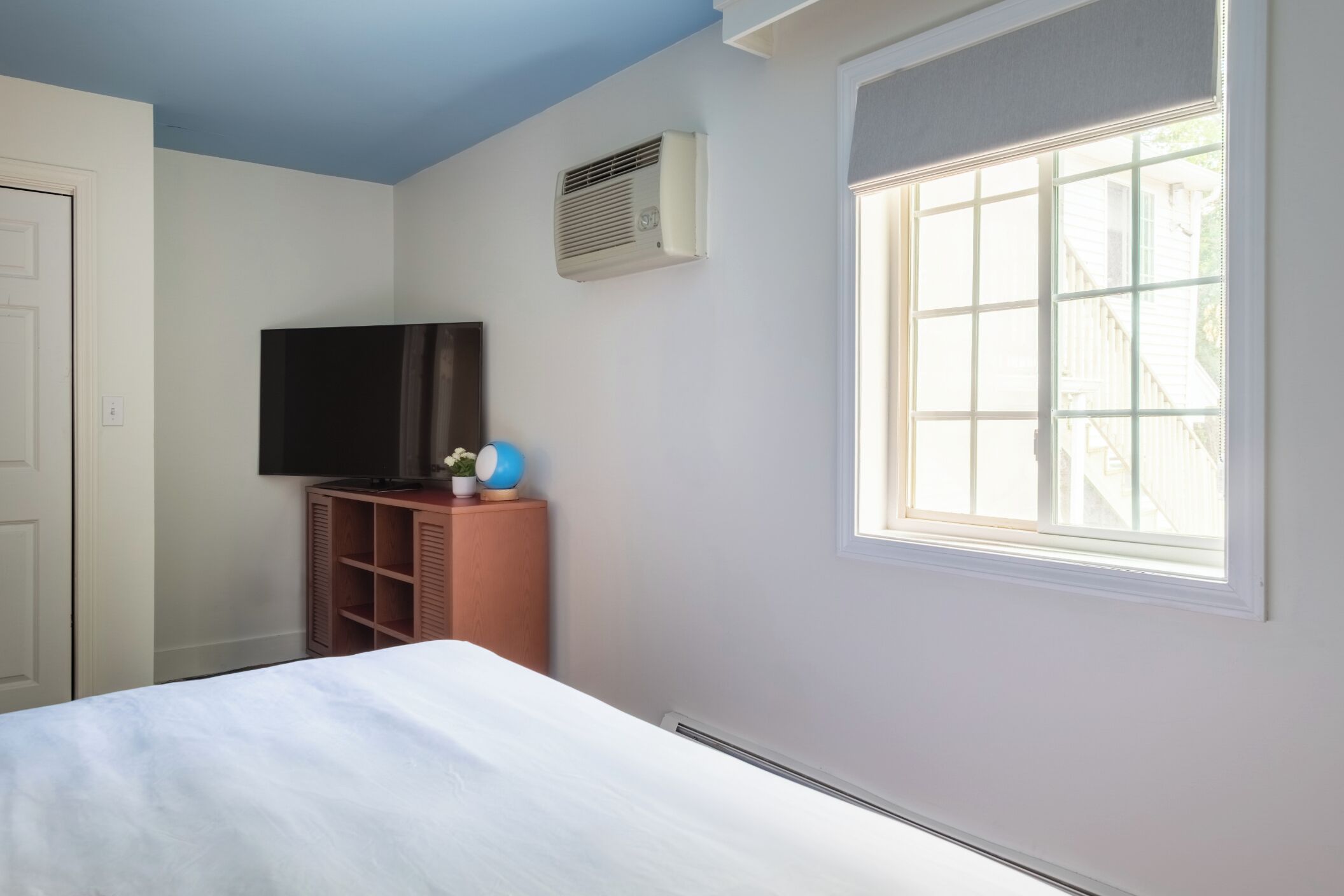 Une chambre à coucher comprenant un lit, un téléviseur, une fenêtre et un appareil de climatisation.