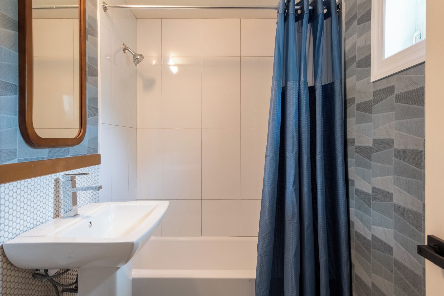 A bathroom with a white sink, a shower with a blue curtain, and tiled walls.