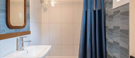 A bathroom with a white sink, a shower with a blue curtain, and tiled walls.