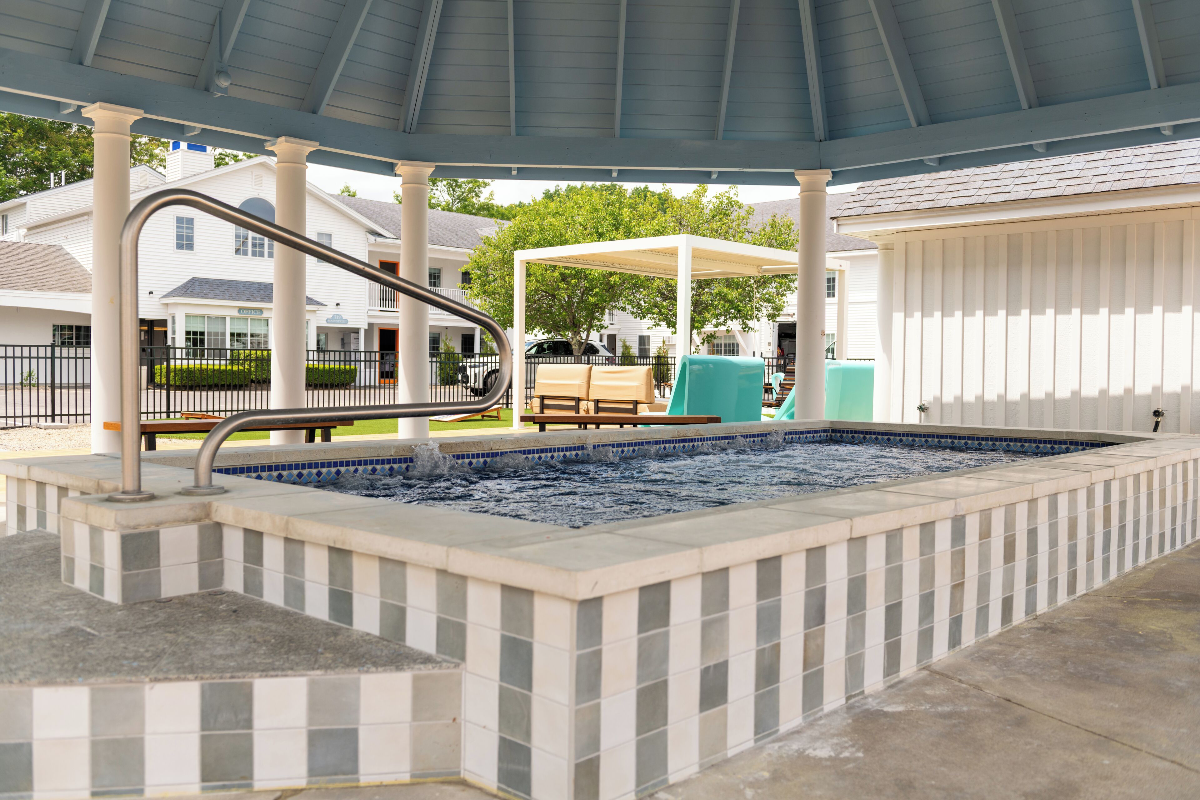 A covered outdoor swimming pool with a tiled deck, a metal handrail, and a bench.