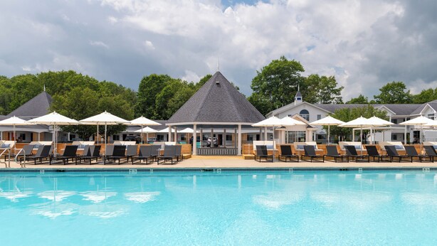 A swimming pool with lounge chairs and umbrellas, surrounded by buildings with a gazebo-like structure. - Driftaway Hotel and Pool (Ogunquit)