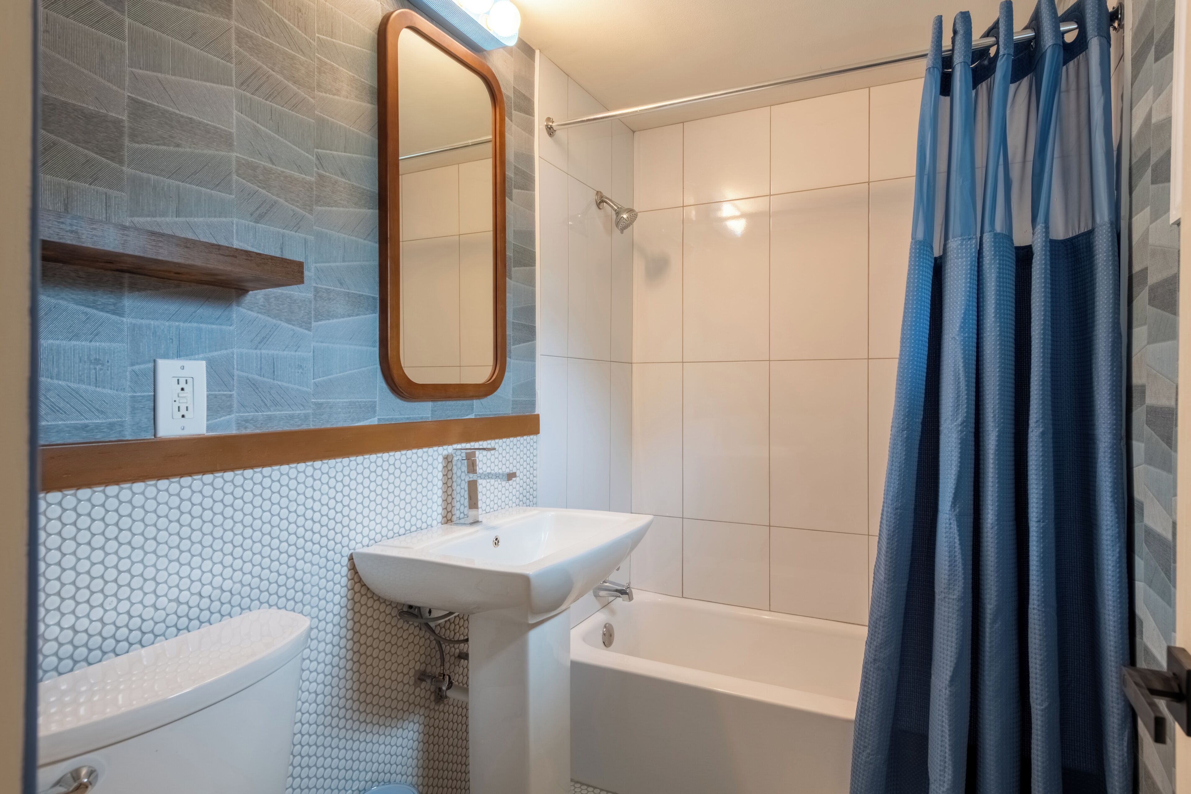 A bathroom with a white sink, a mirror, a shower, and a blue shower curtain.