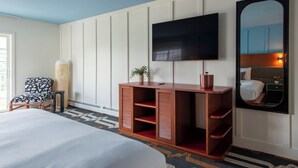 A hotel room with a bed, a TV mounted on the wall, a wooden desk, a chair, and a mirror. - Driftaway Hotel and Pool (Ogunquit)