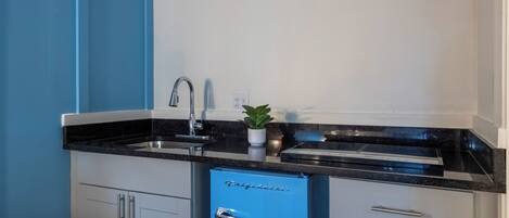 Una cocina compacta con un refrigerador azul, armarios de acero inoxidable, una encimera negra y una pequeña planta en maceta.