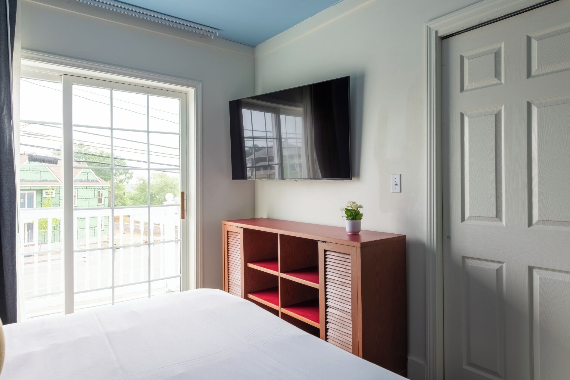 A bedroom with a bed, a wooden cabinet with shelves, a television, and a door.