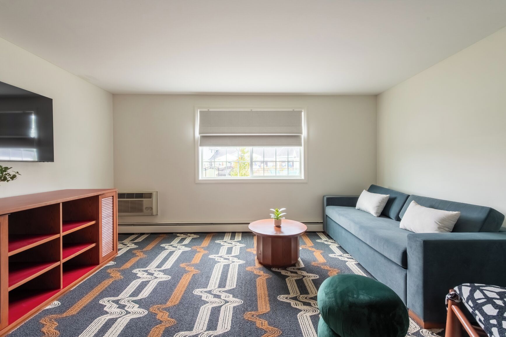 A living room with a sofa, a small table with a plant, a TV mounted on the wall, and a patterned carpet.