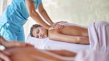 A massage therapy session in a room with a bed and a massage table.