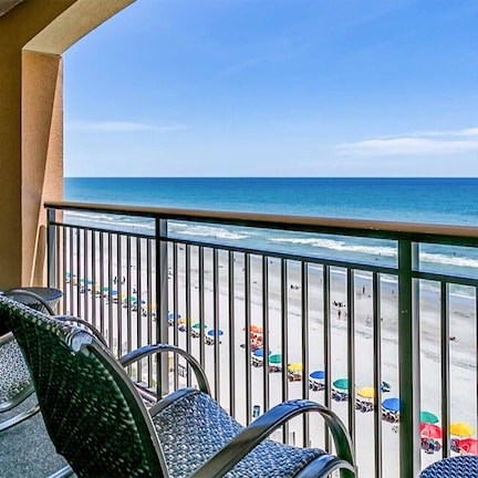 A balcony with chairs overlooking a beach with umbrellas.