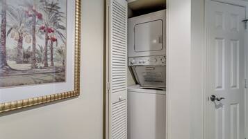 A compact laundry room with a white door, a wall-mounted dryer, and a framed picture of palm trees.