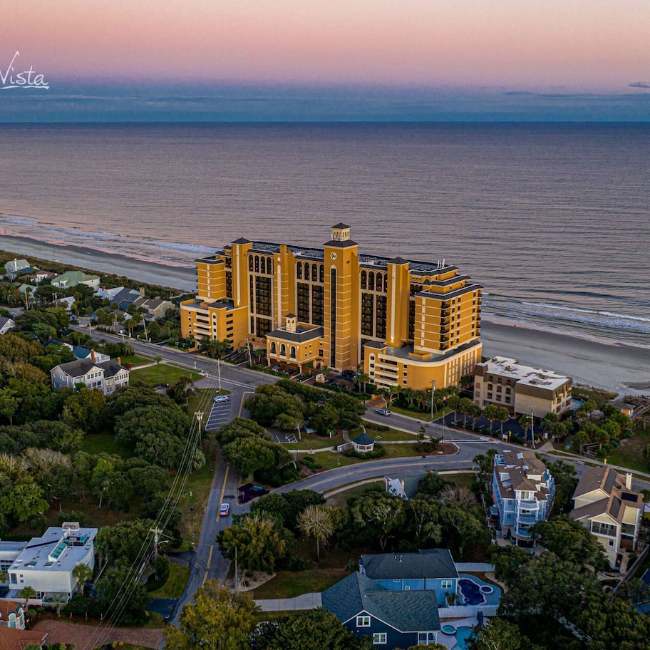 A large, yellow hotel with multiple towers, located near a beach with a view of the ocean.