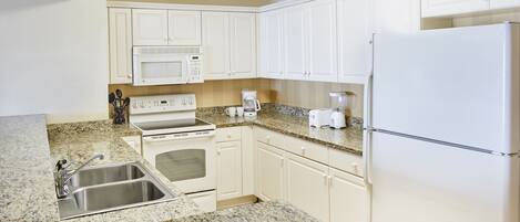 A kitchen with white cabinets, a stainless steel sink, a microwave, a stove, a toaster, and a refrigerator.