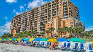 A multi-story hotel with numerous balconies, a beachside location, and a row of beach chairs under colorful umbrellas. - Island Vista Resort (Myrtle Beach)
