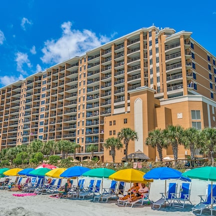 A multi-story hotel with numerous balconies, a beachside location, and a row of beach chairs under colorful umbrellas.