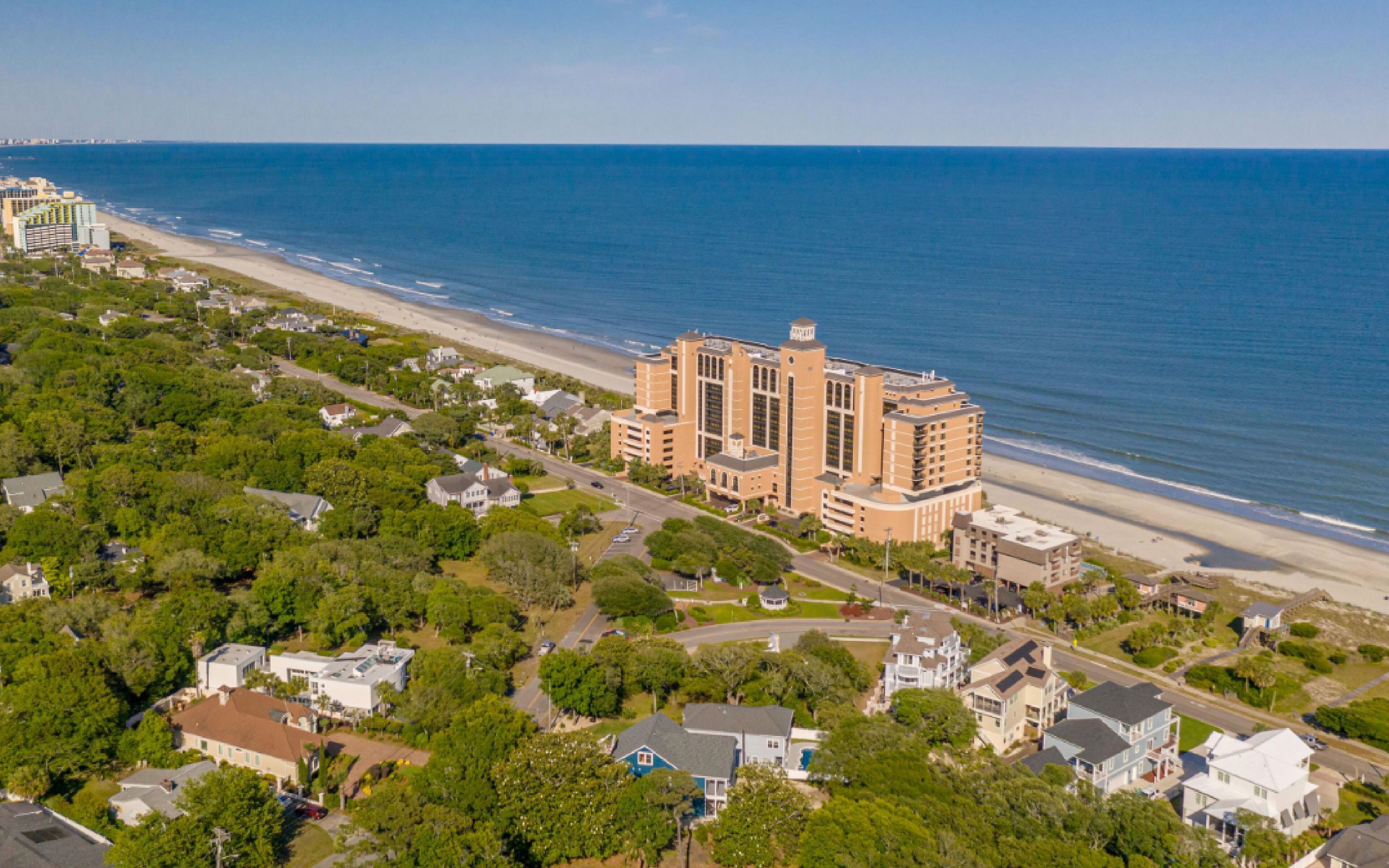 An aerial view of a coastal area with a large hotel complex, a beach, and residential buildings.
