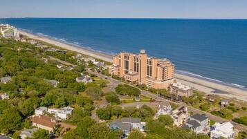 An aerial view of a coastal area with a large hotel complex, a beach, and residential buildings.