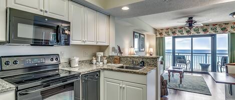 A modern kitchen with stainless steel appliances, white cabinetry, and a large window overlooking a balcony.