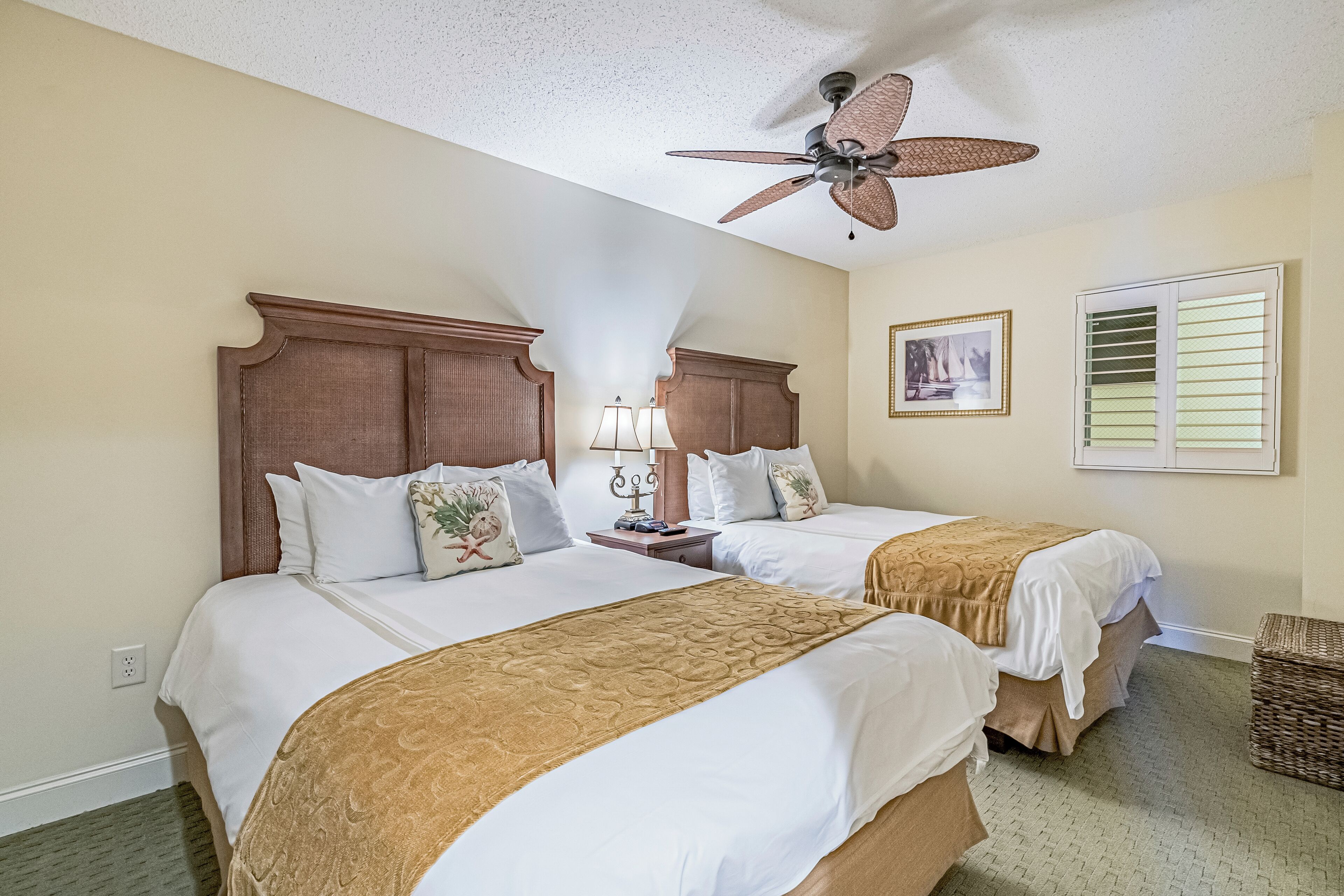 A hotel room with two beds, a ceiling fan, a nightstand with lamps, and a framed picture on the wall.