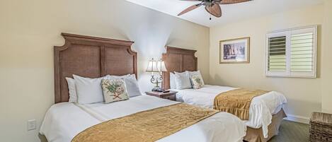 A hotel room with two beds, a ceiling fan, a nightstand with lamps, and a framed picture on the wall.