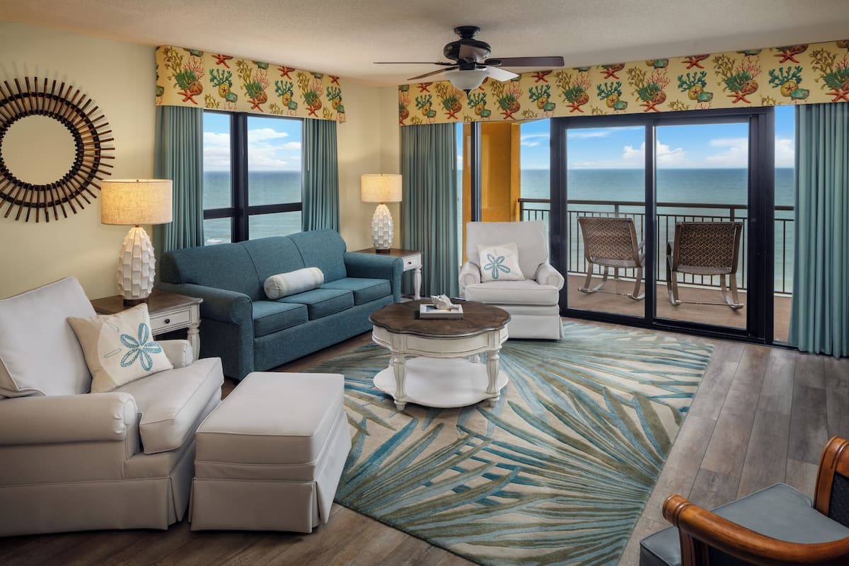 Habitación de hotel con sofá, sillón y una pequeña mesa. Se ve el océano a través de amplias ventanas.