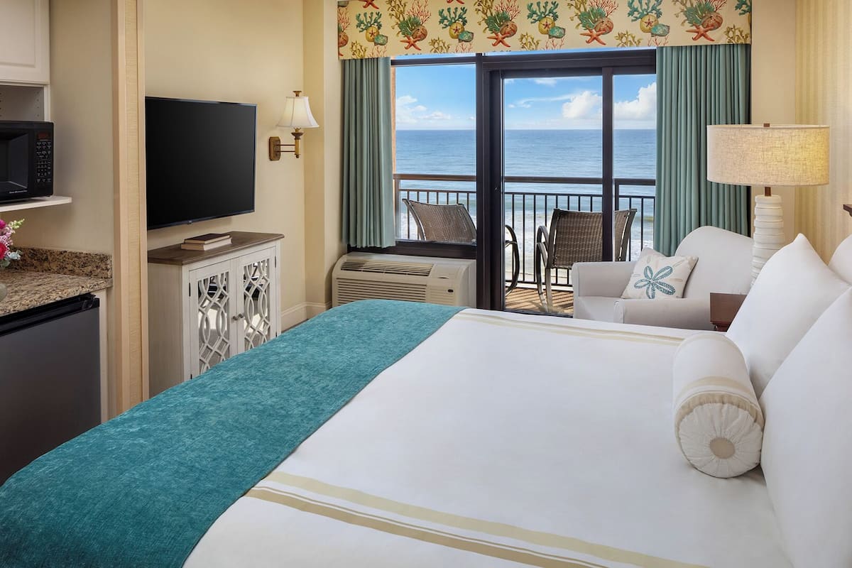 Habitación de hotel con cama, televisión, escritorio con microondas y vista al océano.