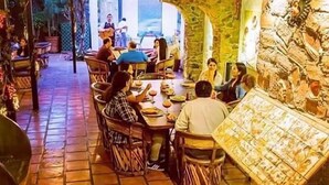 Een restaurant met betegelde vloer en stenen muren, met een centraal eetgedeelte met tafels en stoelen.