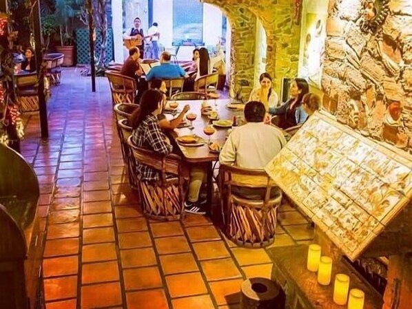 Un restaurante con suelo de baldosas y paredes de piedra, que presenta una zona central de comedor con mesas y sillas.