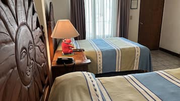 A hotel room with two beds, a wooden headboard, a nightstand with a lamp and a telephone, and a window with curtains.