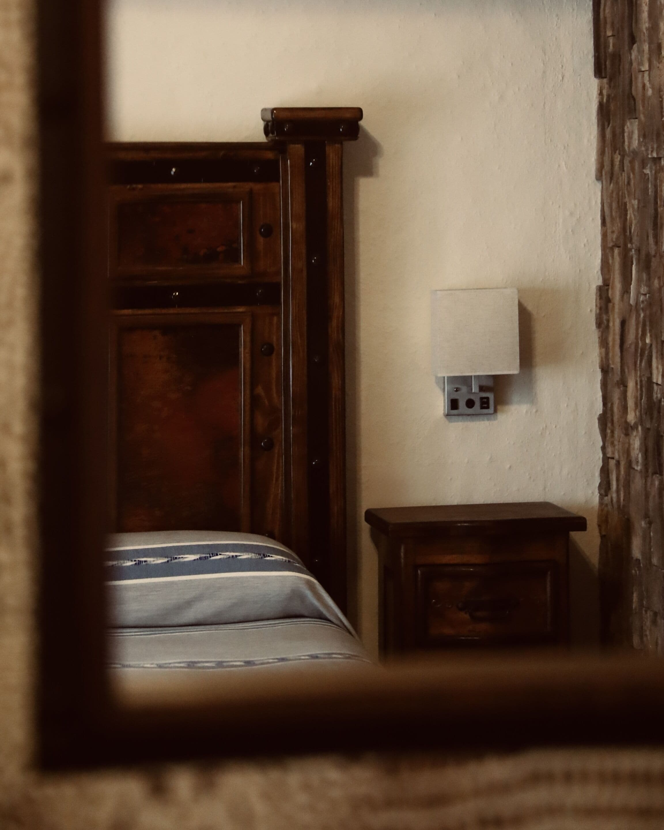 Un dormitorio con una cama de madera, una mesita de noche y una lámpara de pared.