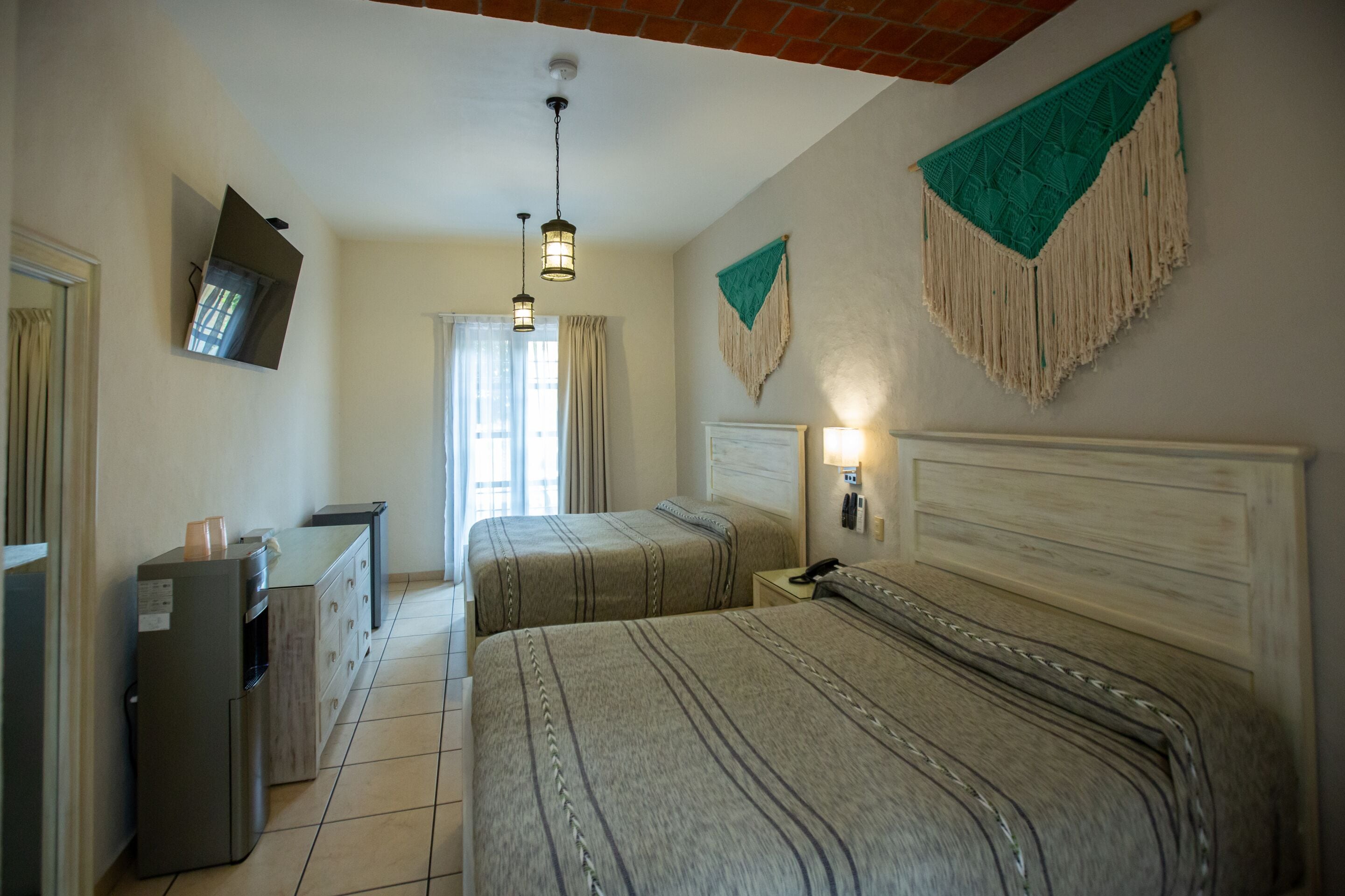 A hotel room with two beds, a desk, a mirror, a TV, and a wall-mounted phone.