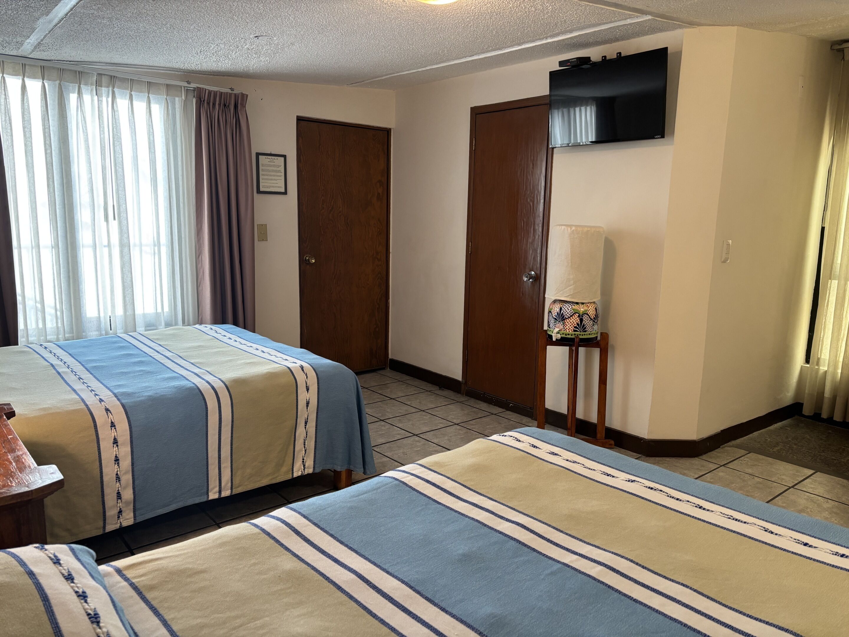 Ein Hotelzimmer mit zwei Betten, einem Holzschrank, einem Fernseher und einem kleinen Tisch mit einer Lampe.