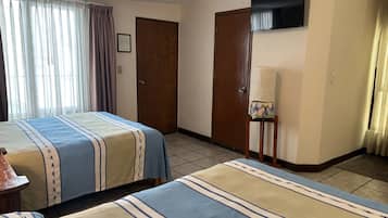 Ein Hotelzimmer mit zwei Betten, einem Holzschrank, einem Fernseher und einem kleinen Tisch mit einer Lampe.