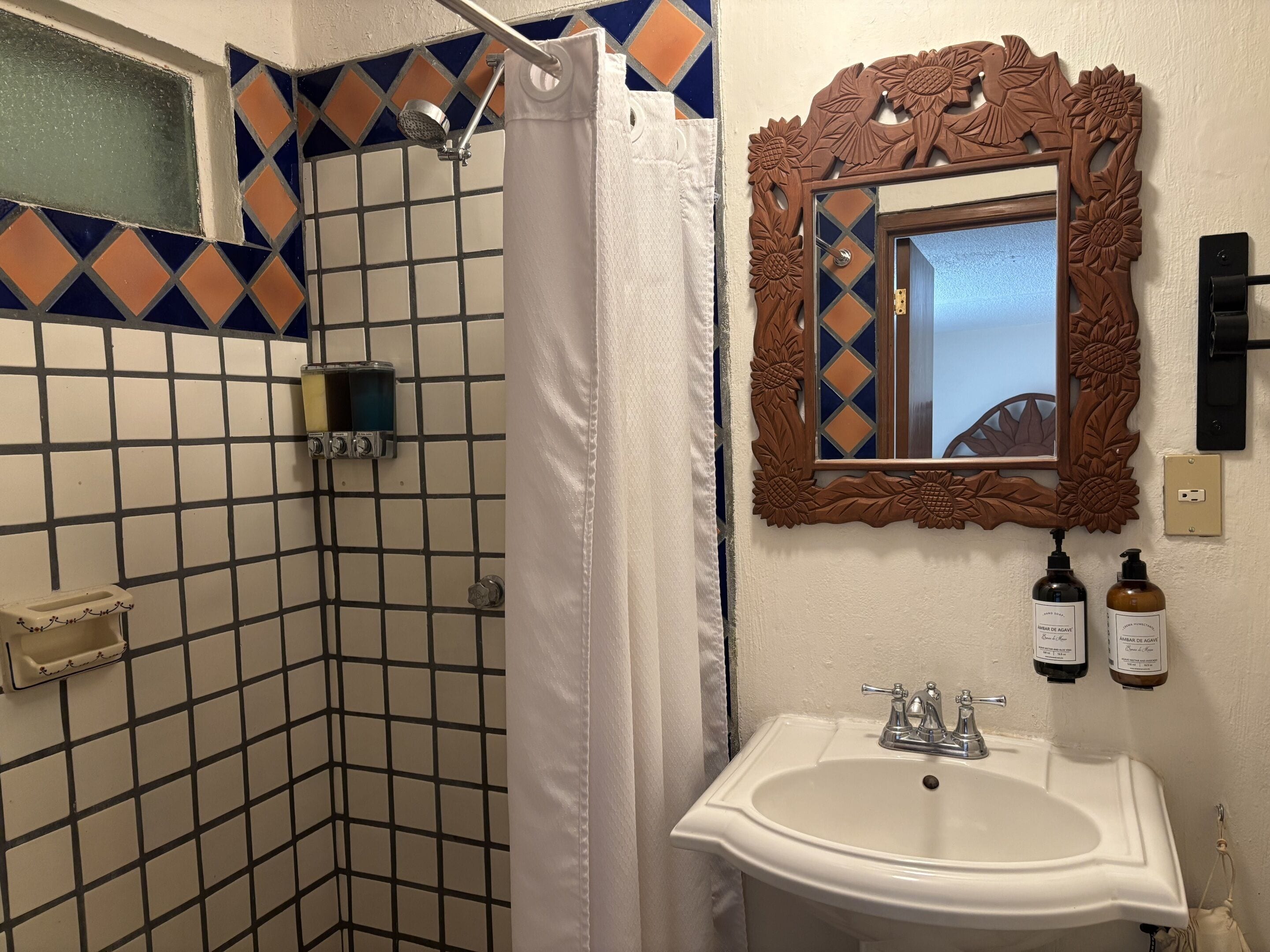 A bathroom with a shower, a sink, and a mirror with floral carvings.