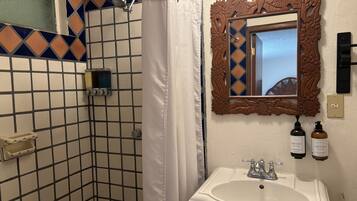 A bathroom with a shower, a sink, and a mirror with floral carvings.