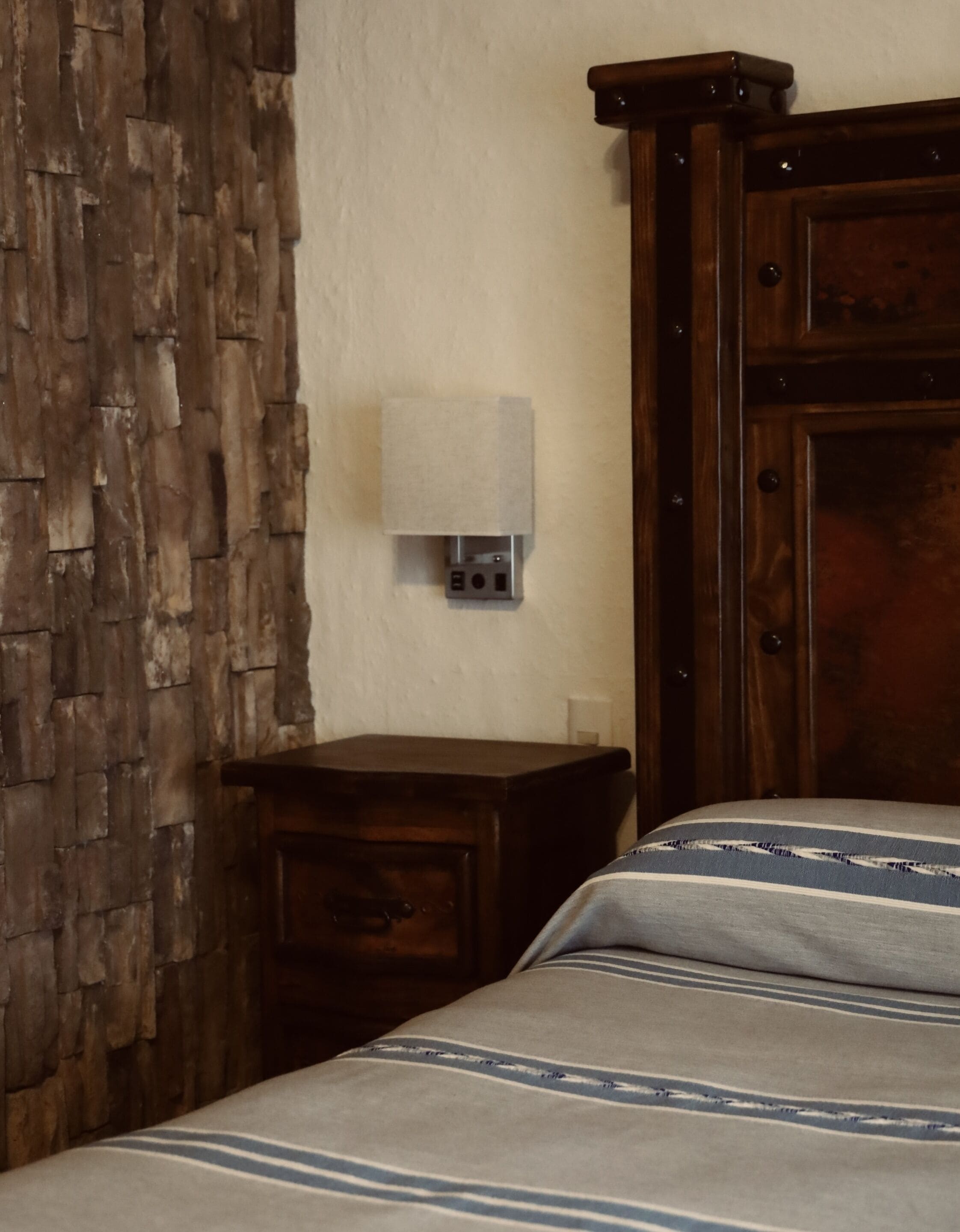 A bedroom with a wooden headboard, a bedside table with a lamp, and a bed with striped bedding.
