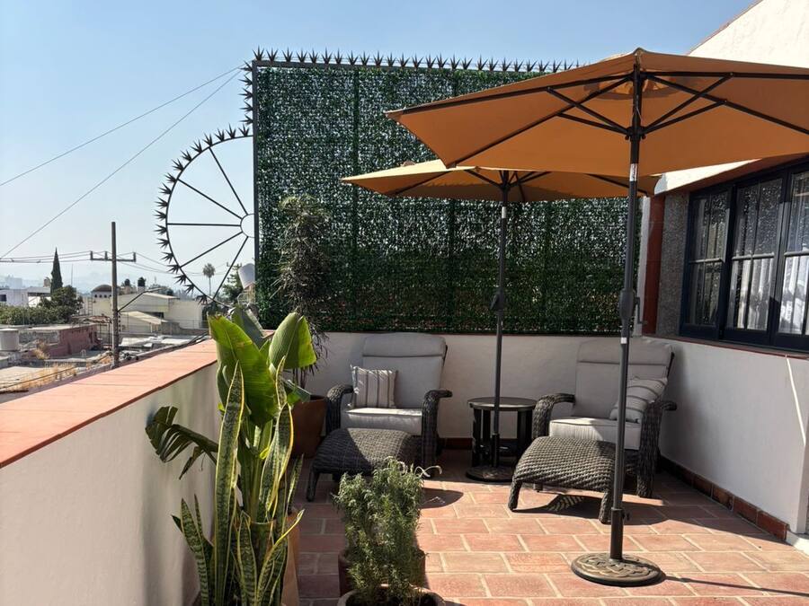 A rooftop terrace with a seating area, potted plants, and a large umbrella.