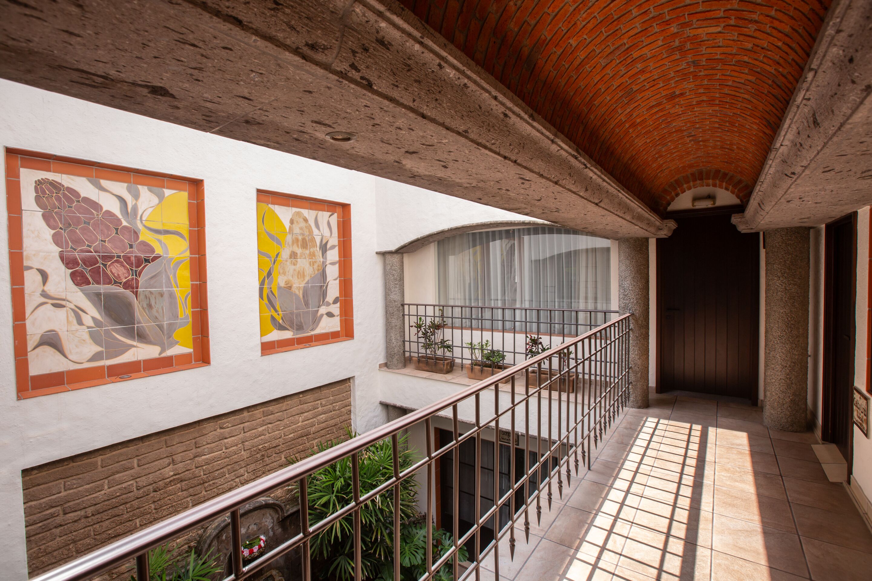 A balcony with a wrought iron railing, a brick wall, and two abstract art pieces on the wall.
