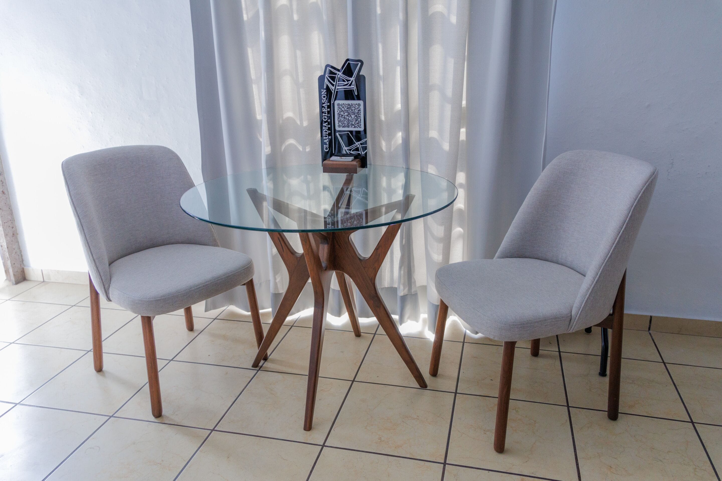 Une pièce moderne avec une table en verre et deux chaises grises recouvertes de tissu.