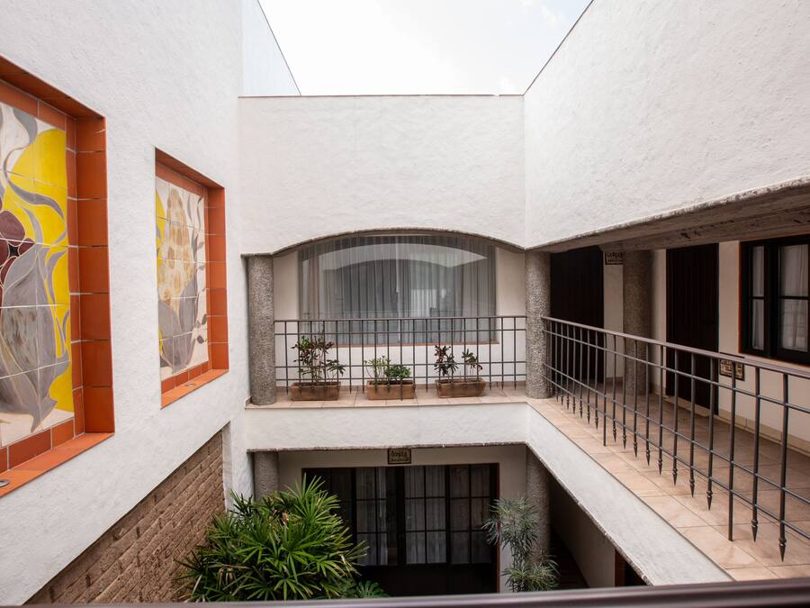 Un interior de varios niveles con un balcón, plantas en macetas y una pared de azulejos con diseño floral.