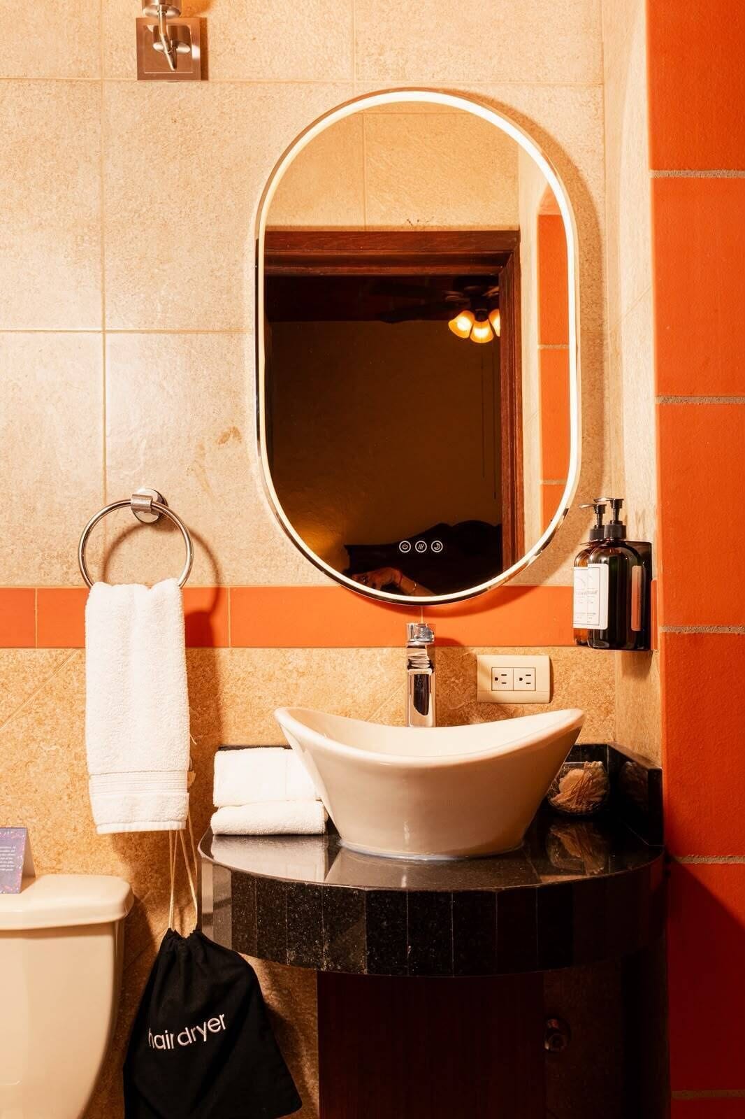 Un baño con un espejo redondo, un lavamanos, un perchero para toallas y una bolsa para secador de pelo.