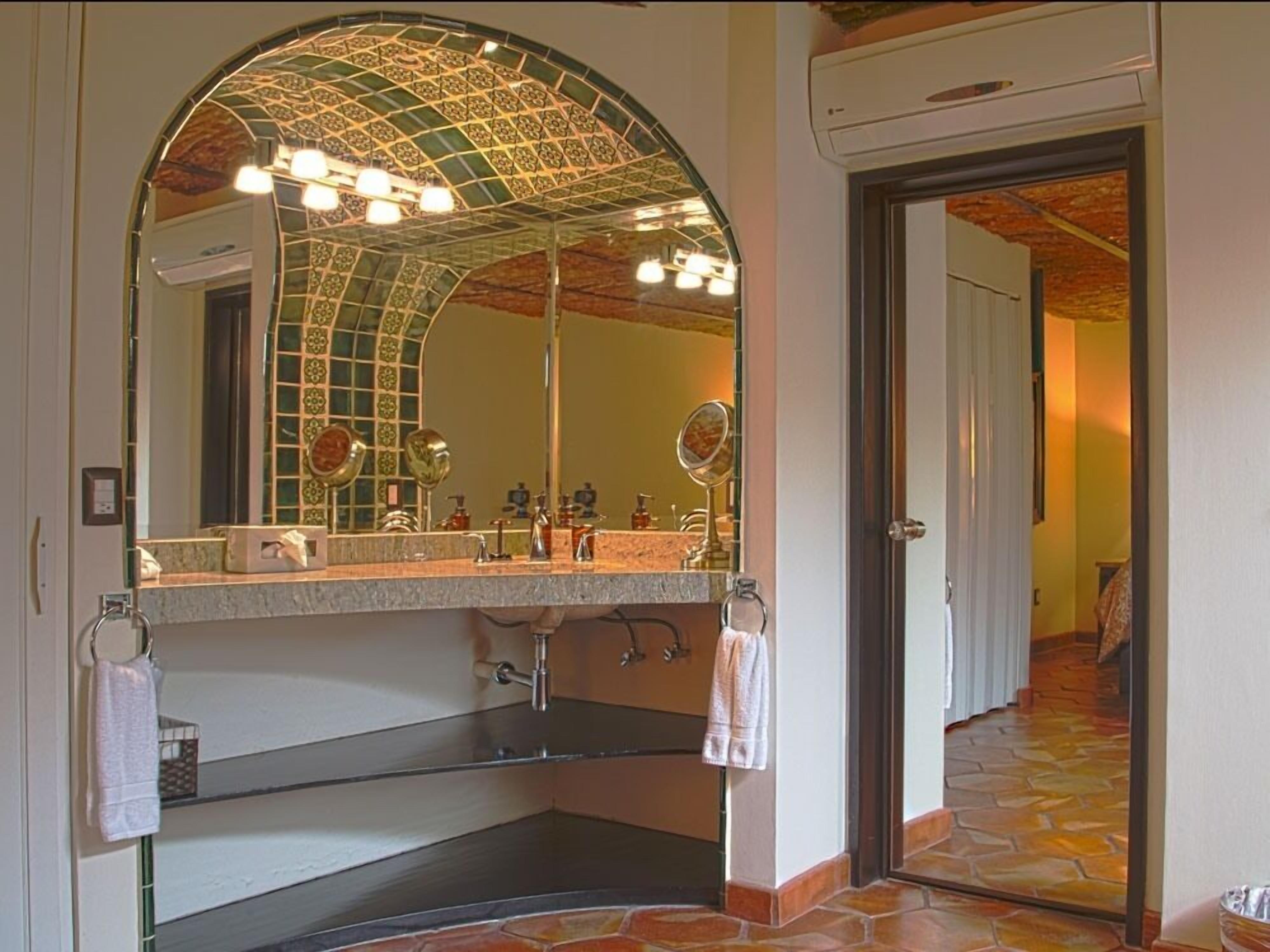 Un baño con un espejo arqueado grande, un lavamanos con toallero y una zona de ducha.
