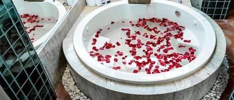 Una bañera circular llena de pétalos de rosa, rodeada por una cuenca de piedra y un piso de baldosas.