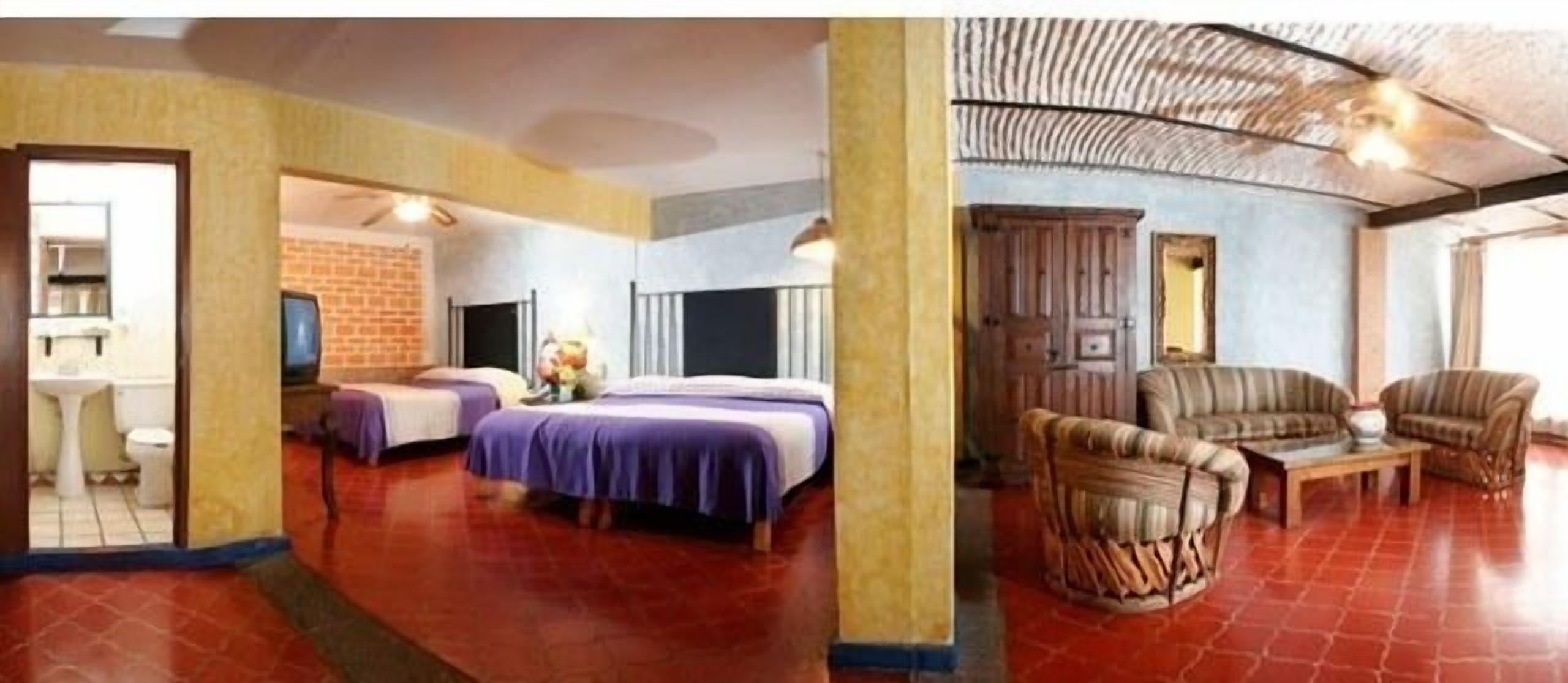 A hotel room with a bed, a sofa, a coffee table, and a television.