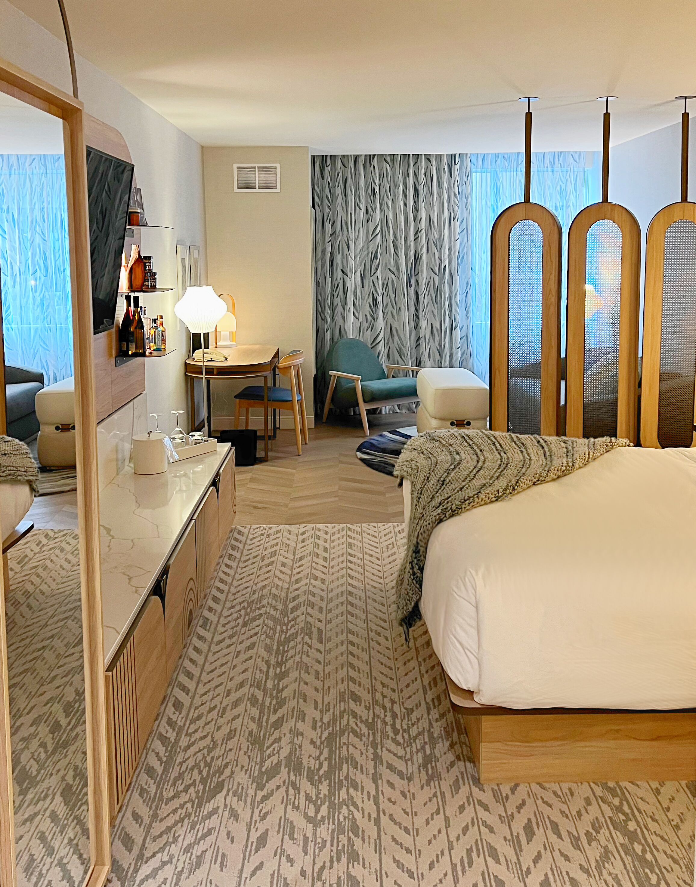 Une chambre d’hôtel comprenant un lit, un bureau avec une chaise, un téléviseur fixé au mur et une fenêtre avec des rideaux.