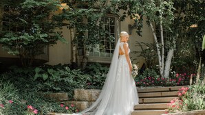 A bride in a white wedding dress with a long veil descending a stone staircase surrounded by lush greenery and flowers. - Hockley Valley Resort (Mono)