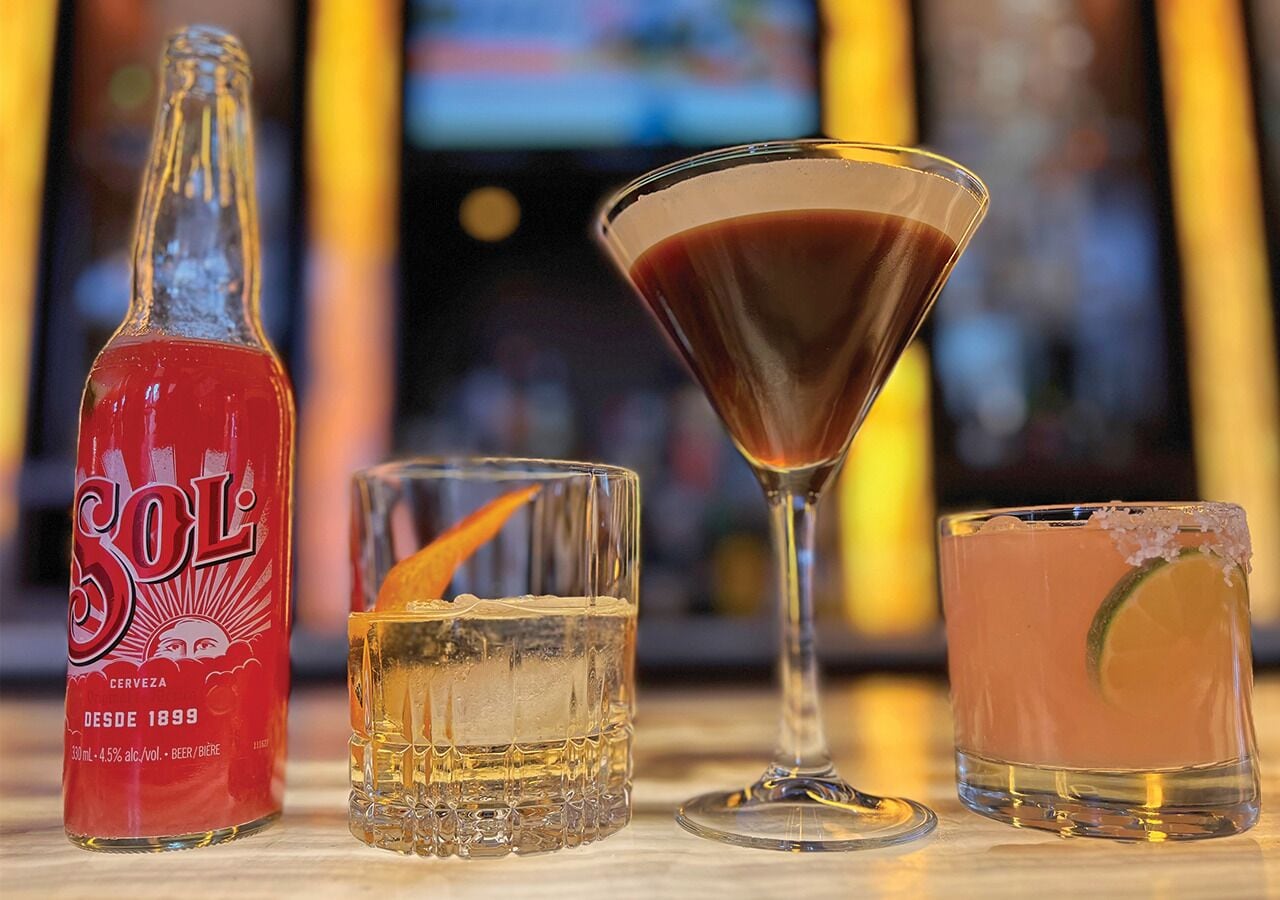 A bottle of Sol beer, a martini glass, a short glass with a lime slice, and a tall glass with ice.